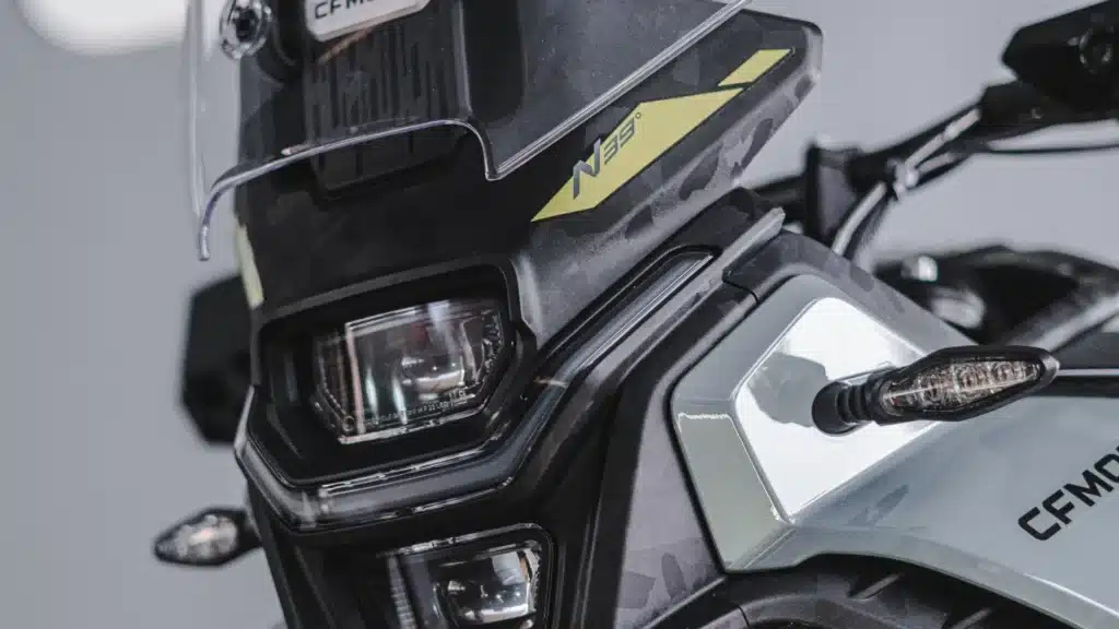 Detalhe do farol e do para-brisa da CFMOTO Ibex 450 cinza.